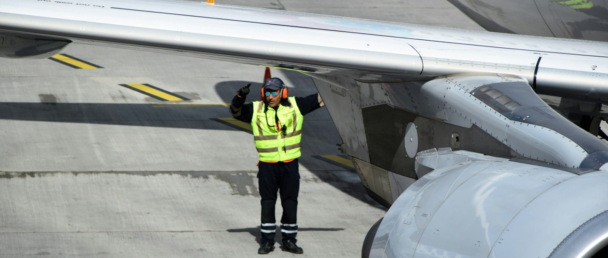 Airport ground crew worker in hi-vis vest and ear defenders marshalling an aircraft on the tarmac